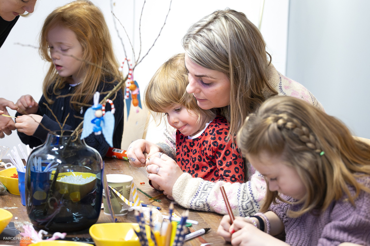 A group of children and an adult engage in a crafting activity at a table, surrounded by art supplies and decorations.