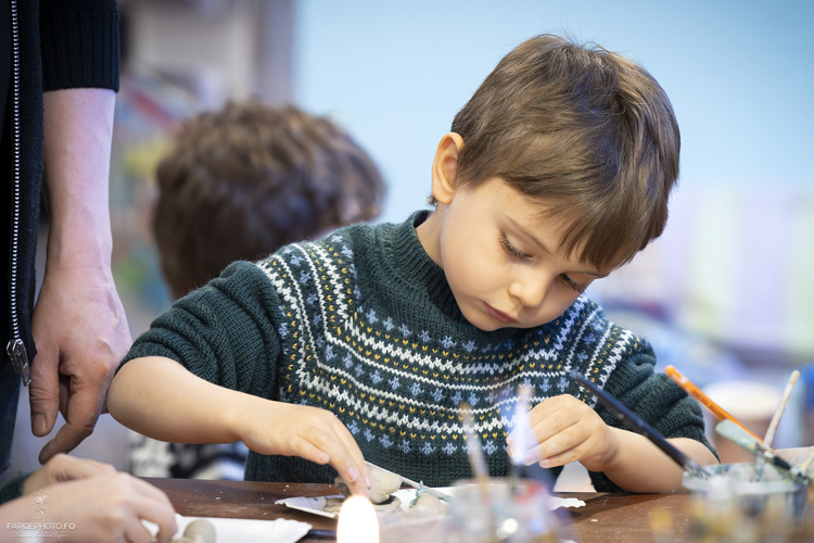 A young child focused on crafting at a table, wearing a patterned sweater, with art supplies around.