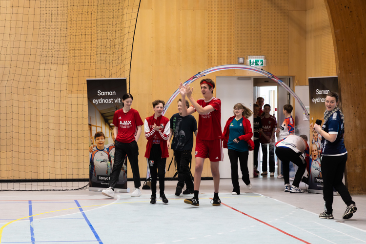 A group of young people in sports attire is entering a gym, celebrating and interacting, with banners in the background.